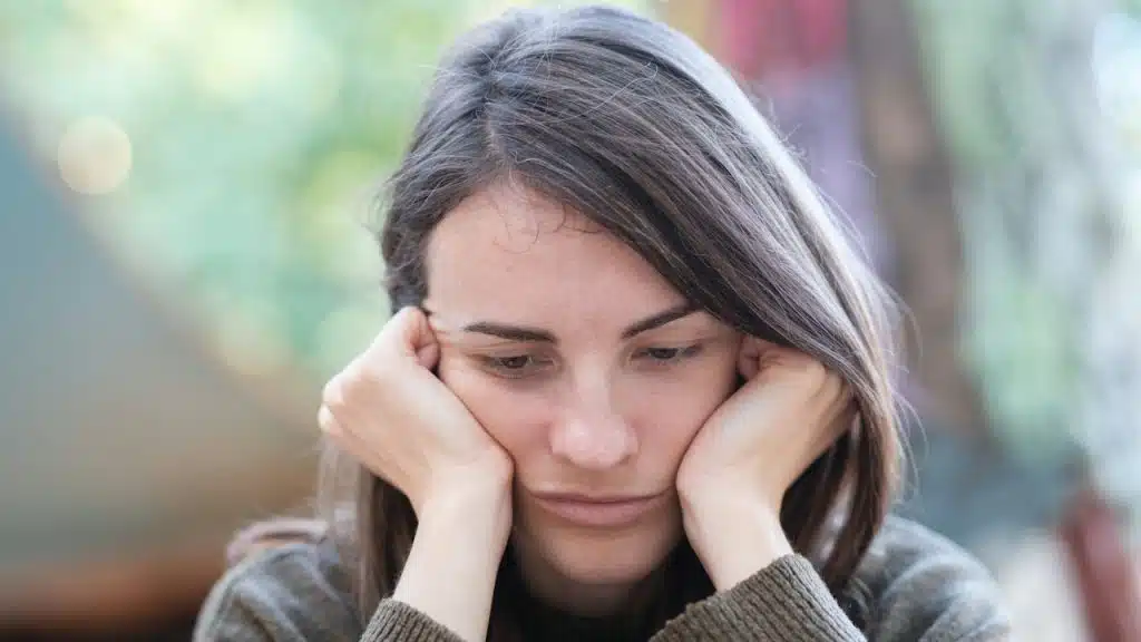 Close-up of a young woman with a sad or disappointed expression, resting her head on her hands.