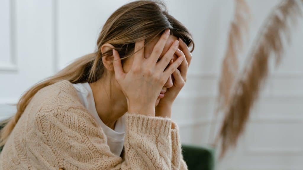 A distressed woman covers her face with her hands.