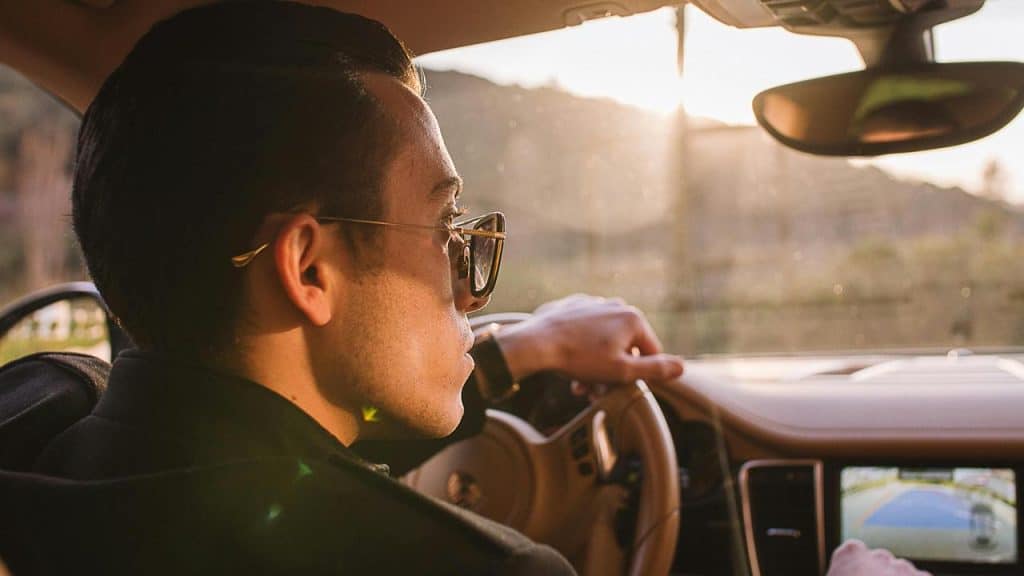 A man wearing sunglasses driving a car with sunlight streaming through the window.