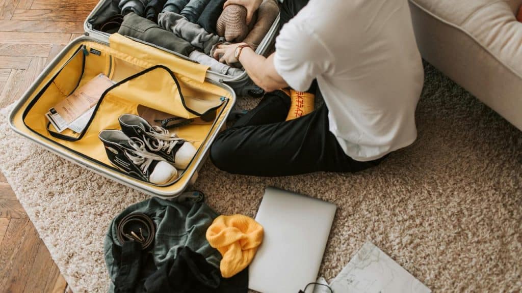 A person packing clothes and shoes into a suitcase on the floor.