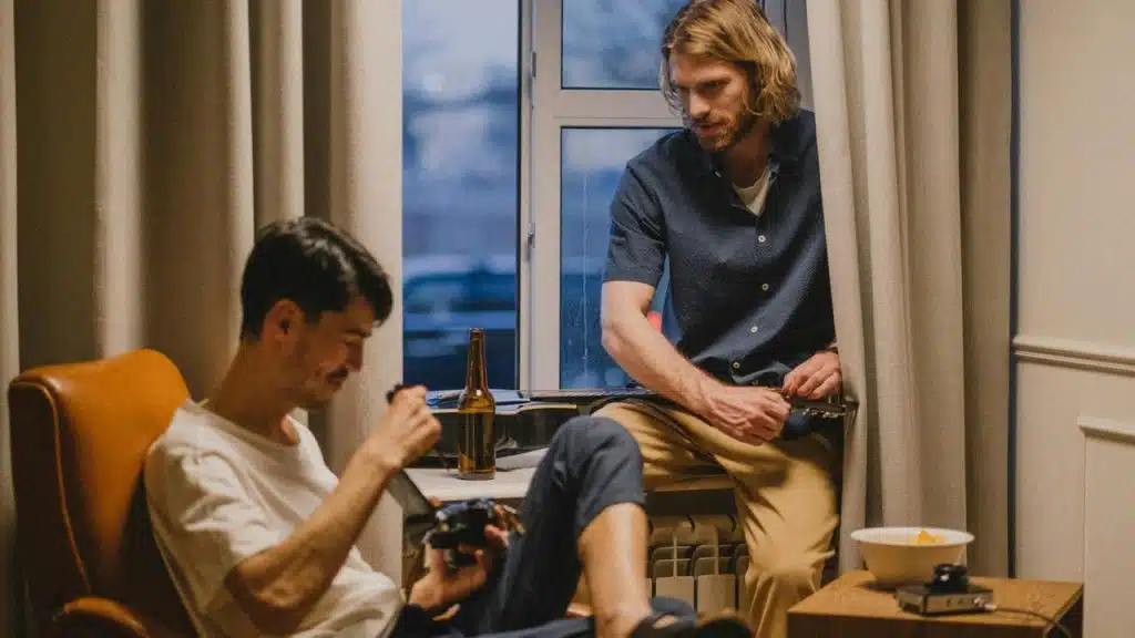 A man with a camera sitting while another leans on the window.