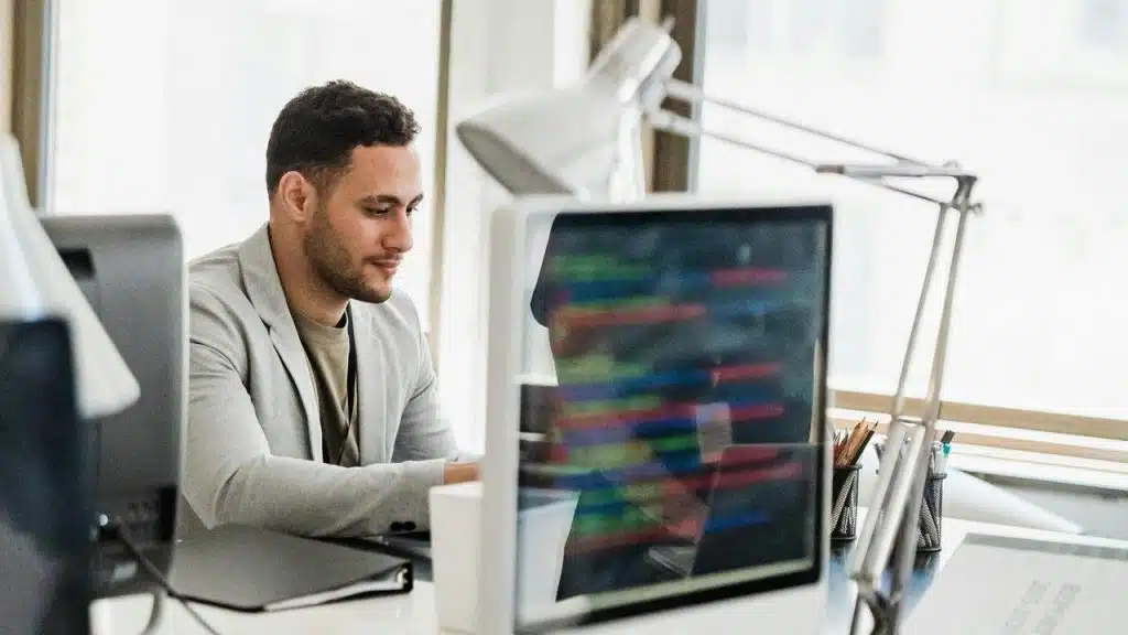 A man in a gray blazer working at a computer in an office.