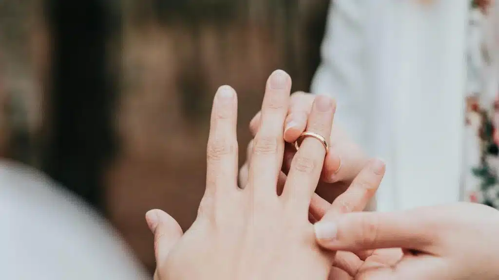 A close-up of one person sliding a wedding ring onto another’s finger.