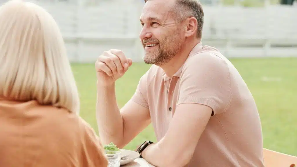 A man smiling while talking with a woman at an outdoor table.