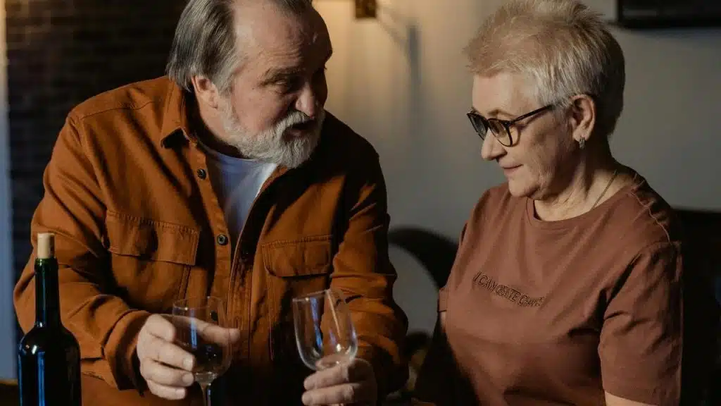 An older couple holding wine glasses and talking warmly indoors.