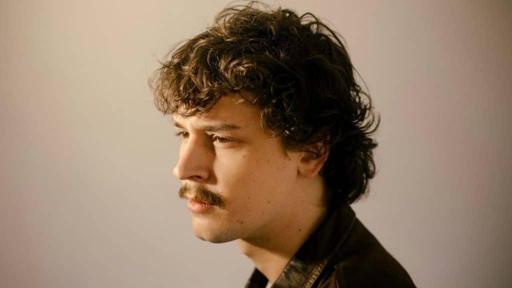 Close-up profile of a young man with curly brown hair and a mustache.