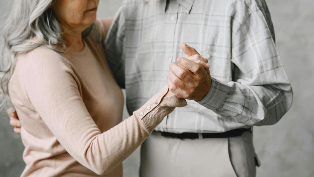An older couple holding hands while slow dancing together.