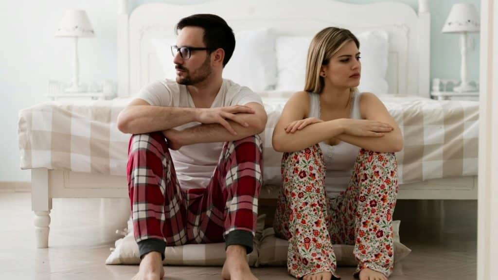 Man with dark hair and glasses looking left while a woman looks right, sitting side-by-side in pajamas.