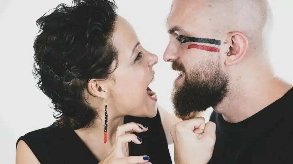 Man and woman yelling at each other; man has red and black face paint.