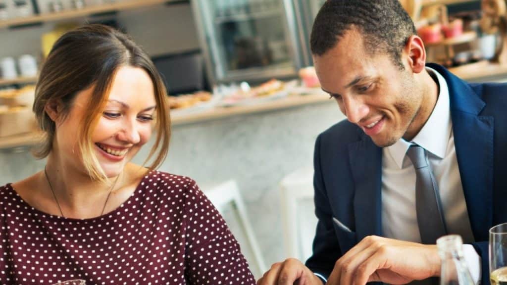 Man and woman smiling at each other while seated at a table in a cafe.