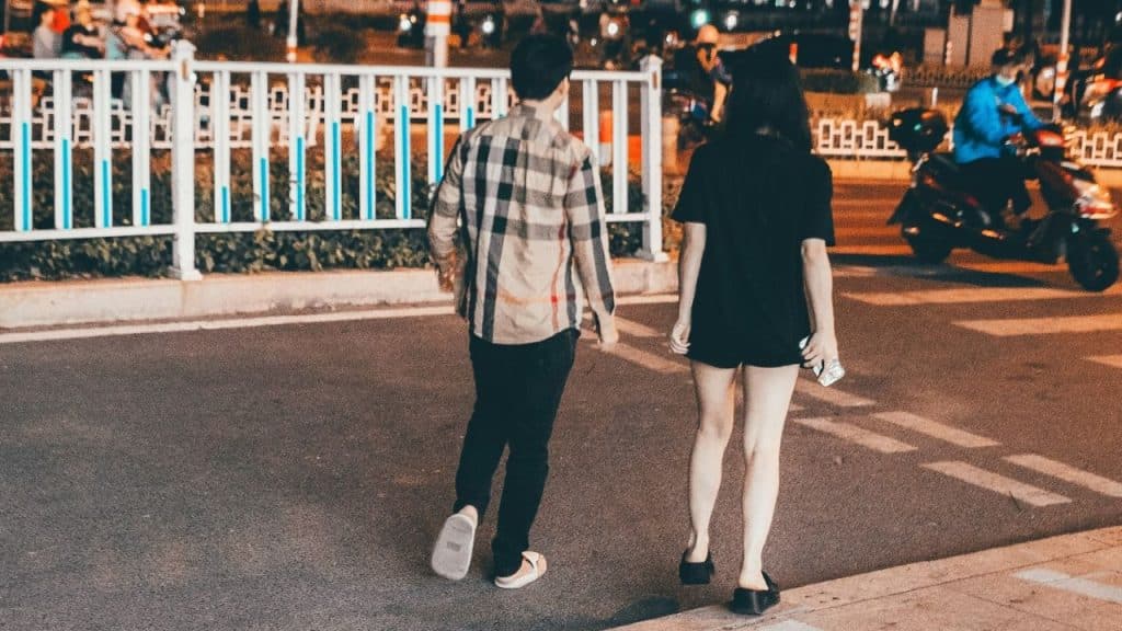 A man and woman walk away from the camera on a city street at night.