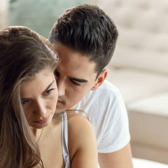 Man in white shirt leaning close to a woman with long brown hair in a living room.