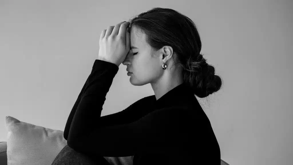 Woman with a serious expression and hands covering her face, in black and white.