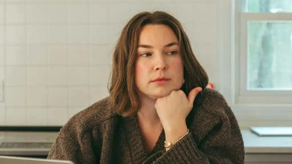 Woman with brown hair resting her chin on her hand, looking away in a kitchen.