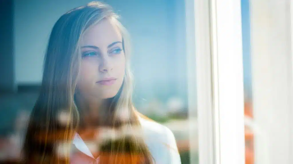 Young woman with blonde hair looking through a window with a blue reflection.
