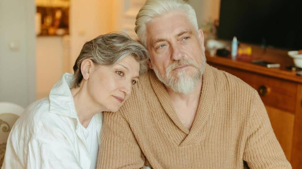 An older couple sitting closely with the woman resting her head on the man’s shoulder.