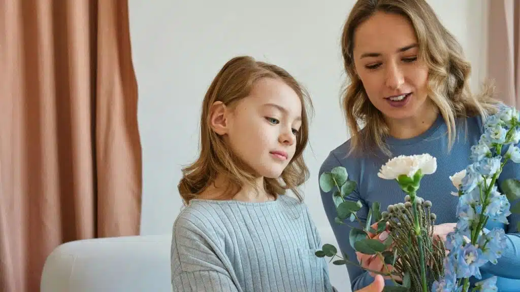 A woman and a young girl arranging flowers together indoors.