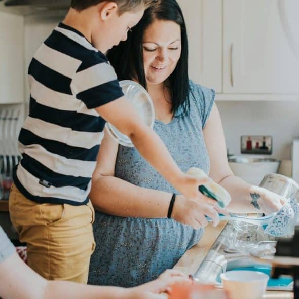 A woman and two children washing dishes together in a kitchen.