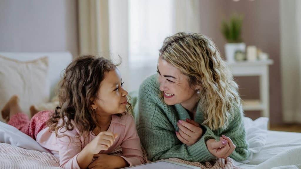 A woman and a young girl lying on a bed smiling at each other.