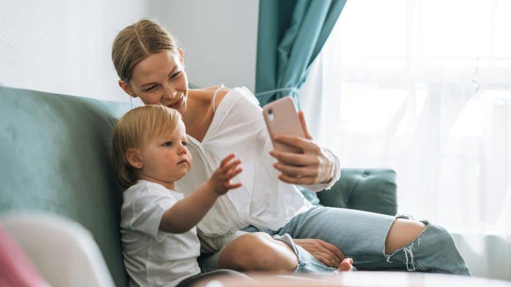 A woman taking a selfie with a small child on a couch.