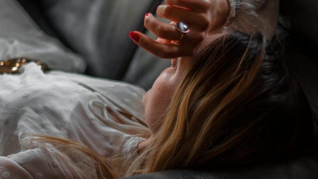 A woman lying on a couch with her hand over her face.