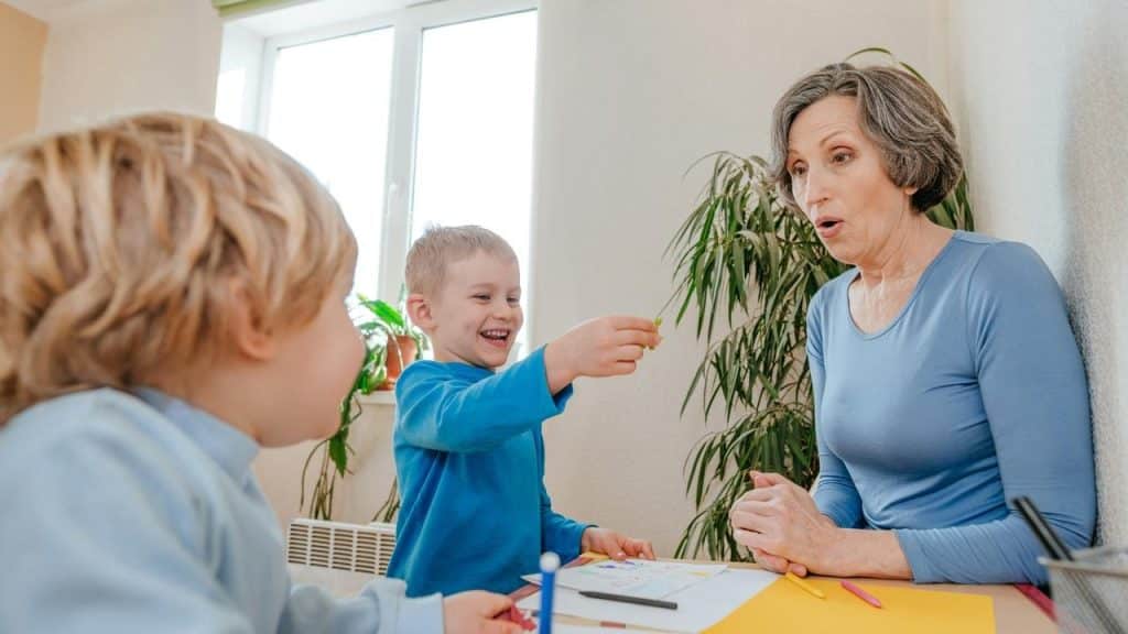 An older woman sitting at a table with two children, looking surprised.