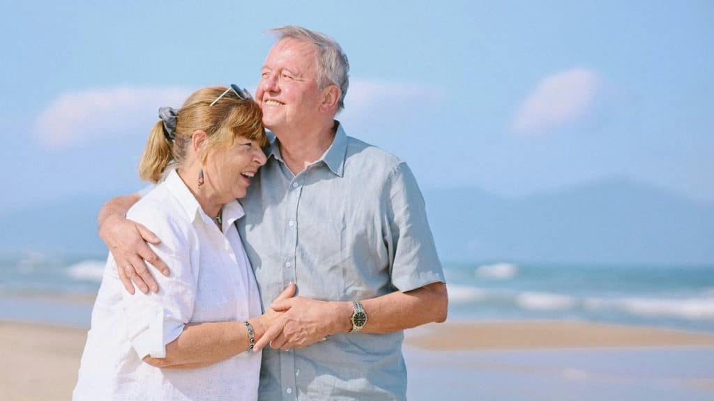 A smiling older couple embracing on a sunny beach.