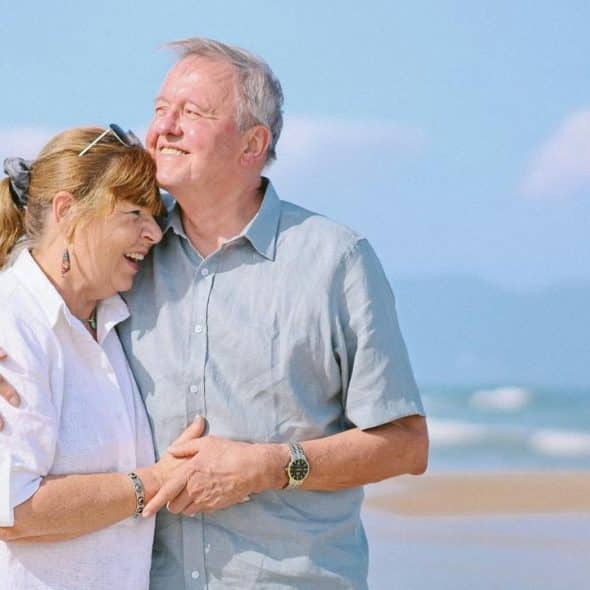 A smiling older couple embracing on a sunny beach.