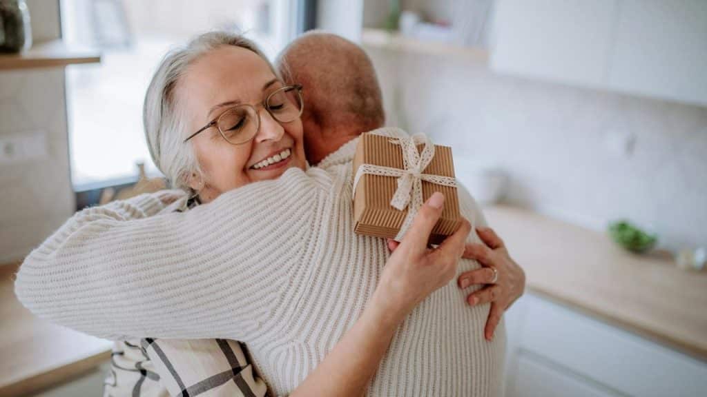 An older woman hugging a man while holding a small wrapped gift.