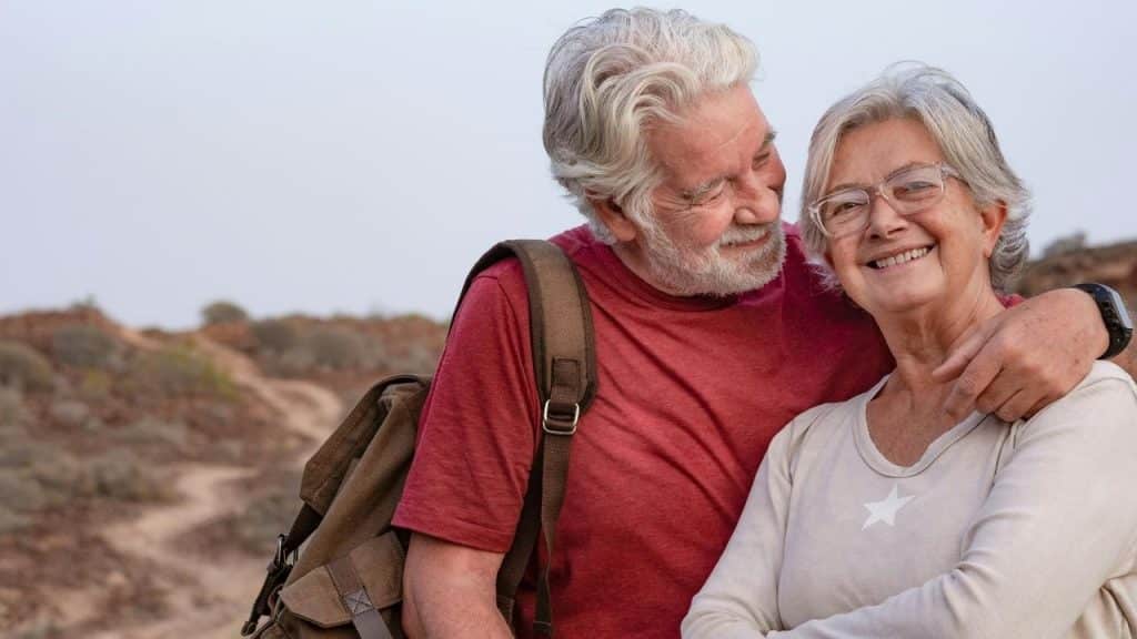 An older couple smiling and embracing while hiking outdoors.