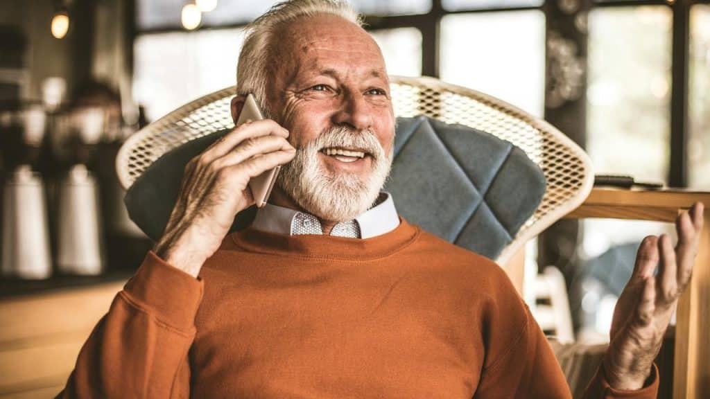 An older man smiling while talking on a mobile phone.