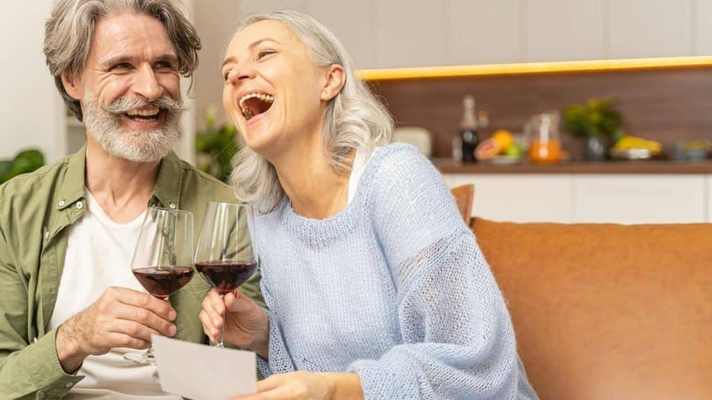 An older couple laughing together while holding glasses of red wine.