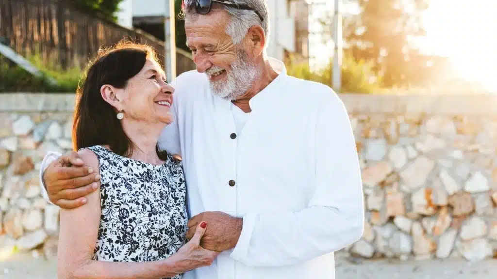 An older couple smiling warmly at each other while embracing outdoors.