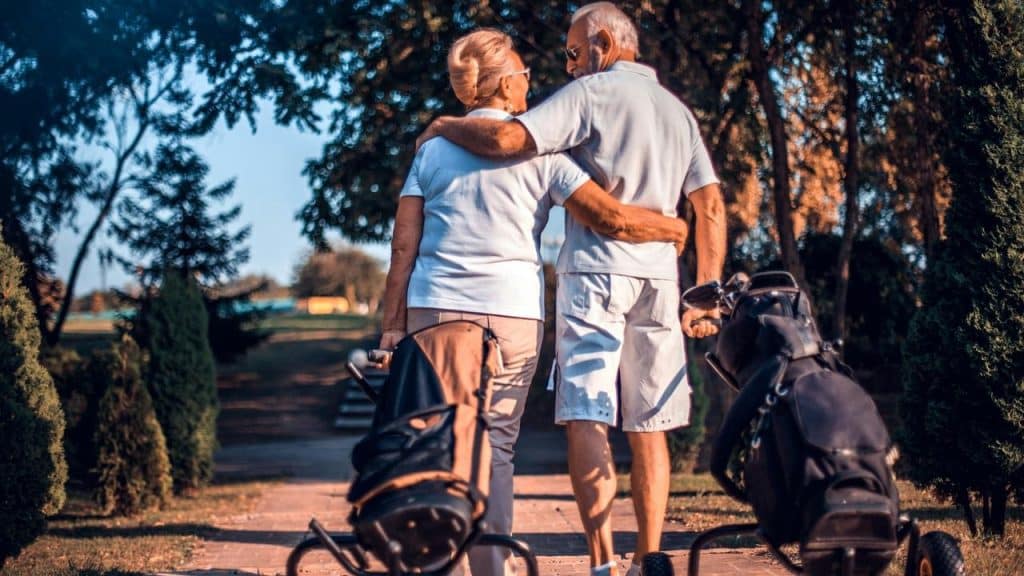 An older couple walking arm in arm with golf bags on a course.