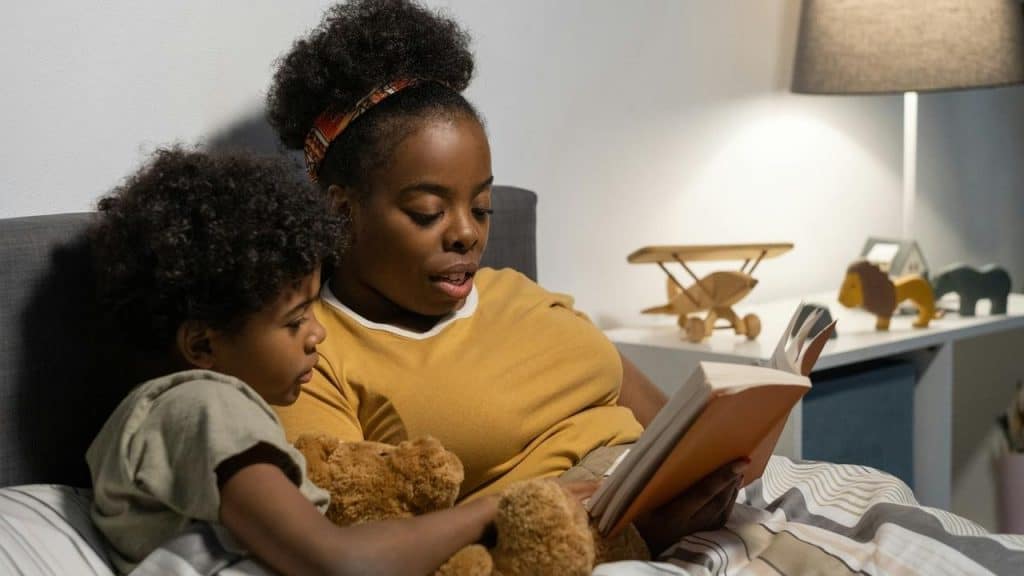 A woman reading a book to a child in bed at night.