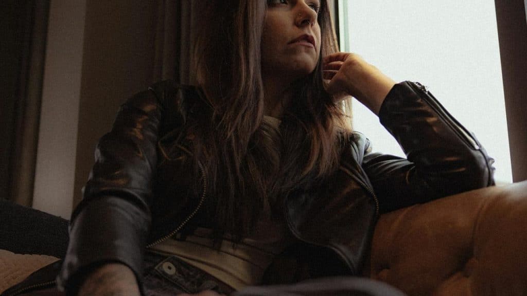 A woman in a leather jacket sitting thoughtfully by a window.