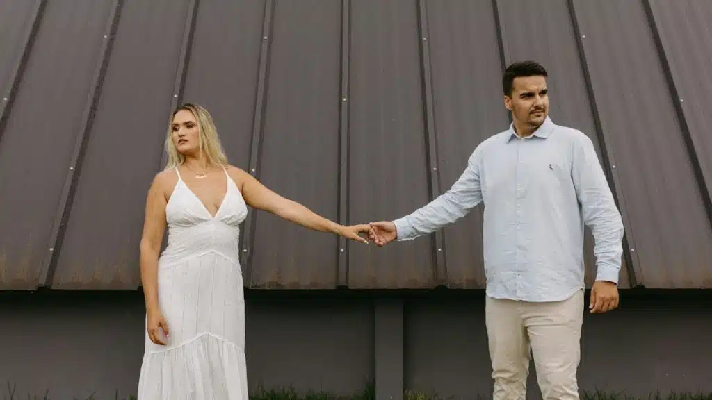 A man and woman holding hands while standing apart and looking in opposite directions.
