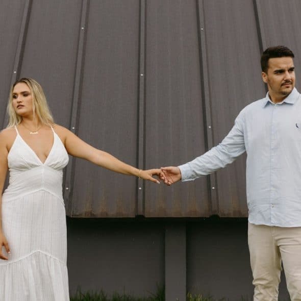 A man and woman holding hands while standing apart and looking in opposite directions.