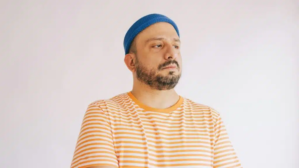 Man with a beard and blue beanie, wearing an orange and white striped shirt.