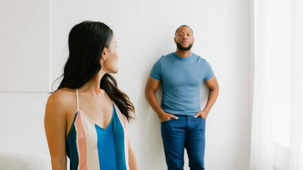 A woman looking back at a bearded man who is leaning against a wall.