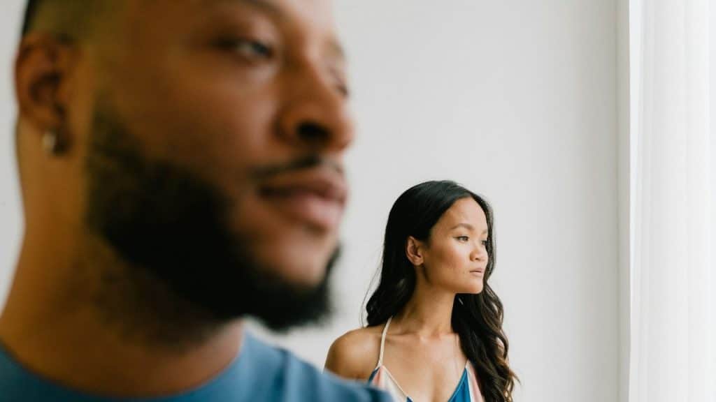 A man's blurry face is in the foreground, and a woman looks away in the background.