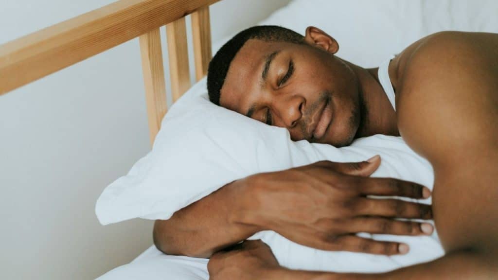 A man is sleeping in bed on a white pillow, hugging a pillow to his chest.