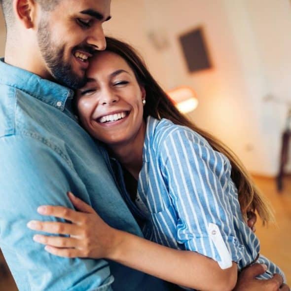 Smiling couple embracing affectionately inside a brightly lit room.