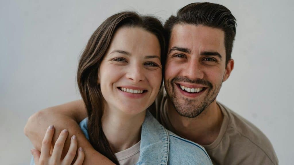 Smiling man with beard and woman with long hair embracing and looking at the camera.