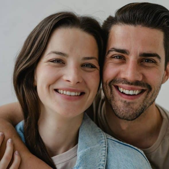 Smiling man with beard and woman with long hair embracing and looking at the camera.