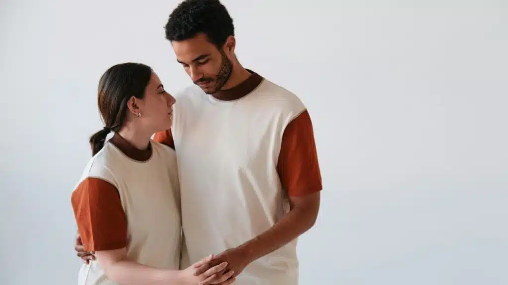 Man and woman in matching shirts hold hands, looking at each other against a white background.