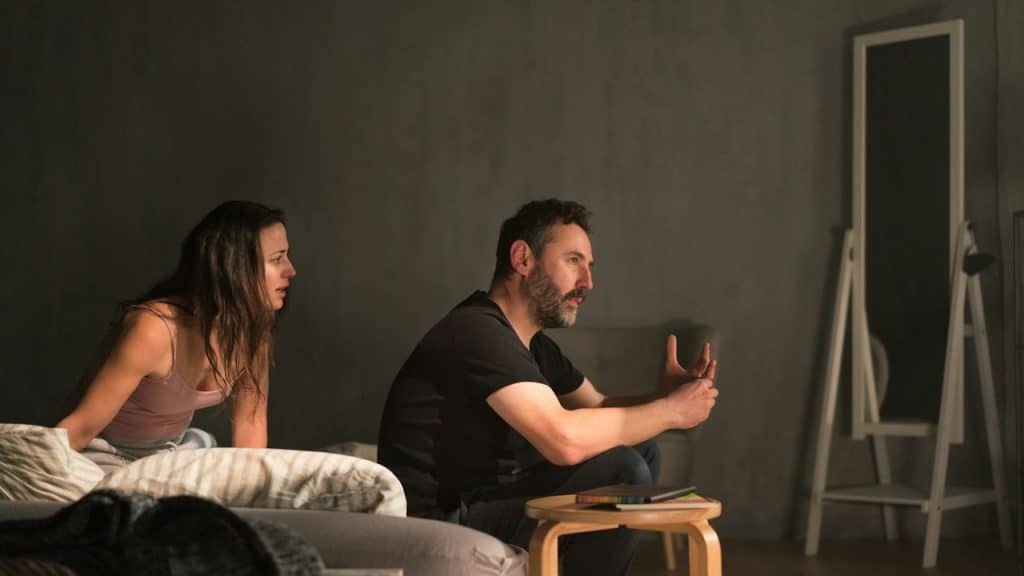A woman talking to a man who has his back turned to her and refuses to answer as they sit on a bed.