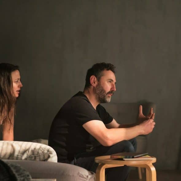 A woman talking to a man who has his back turned to her and refuses to answer as they sit on a bed.