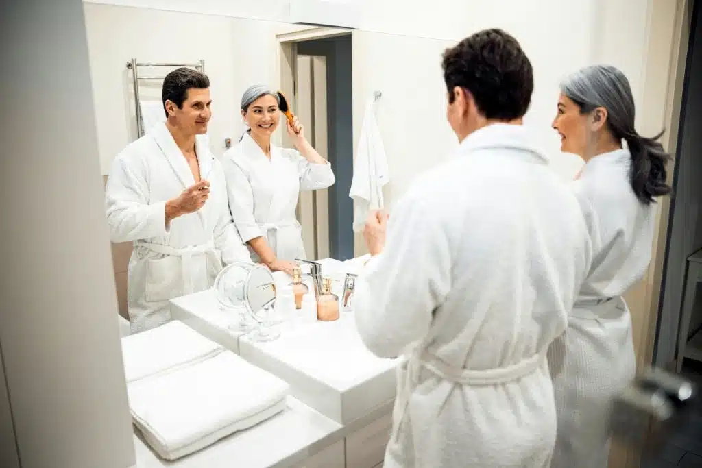 A mature couple wearing bathrobes and looking at the mirror while getting ready in the morning.