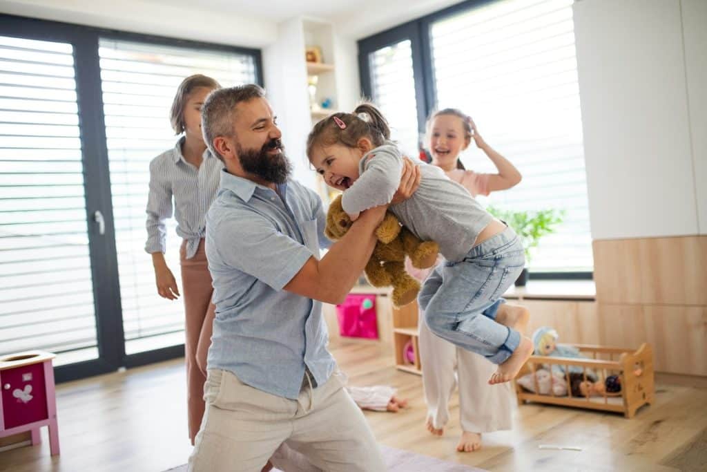 A father playing with his three daughters at home.